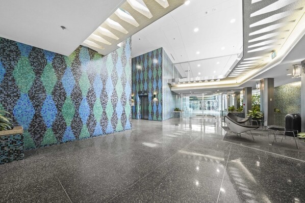 Un hall d’entrée spacieux, doté d’un sol poli, d’un mur orné de motifs et de luminaires modernes.