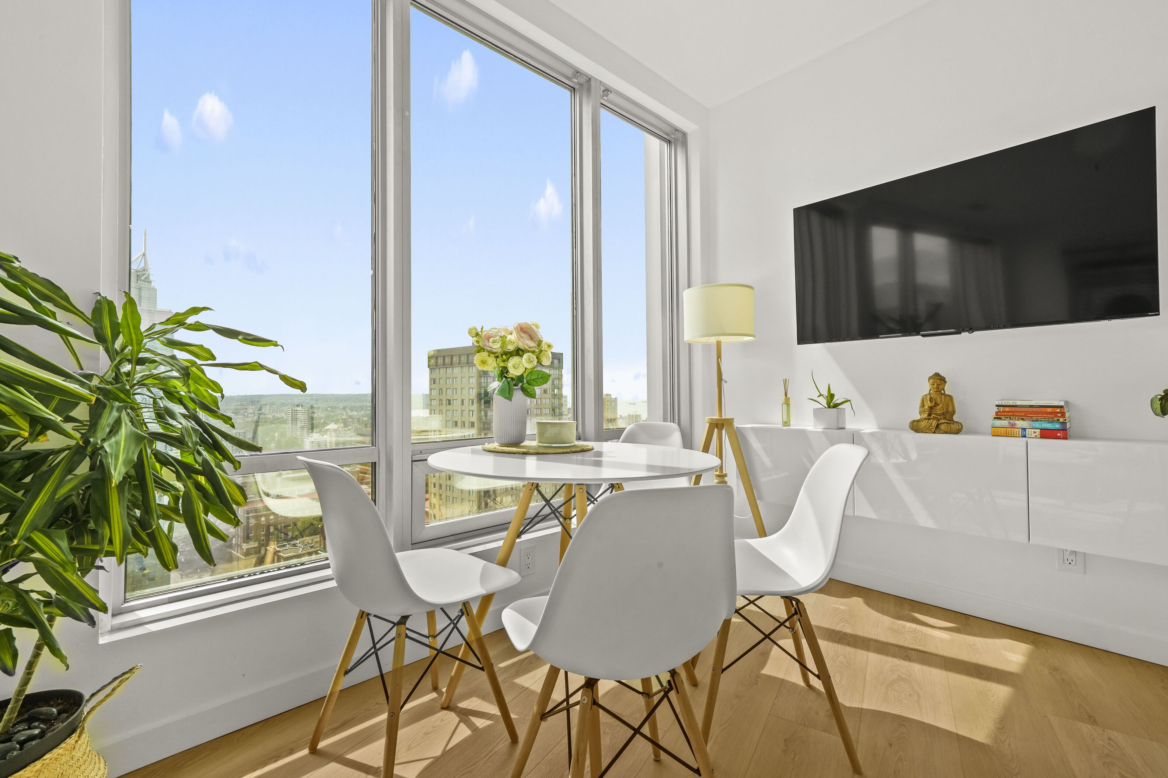 A modern dining area with a round table, white chairs, and a view of a cityscape through large windows.