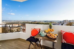 Enjoy a city view from this balcony with a table set for a relaxing morning, featuring a bowl of fresh fruit, pastries, and a refreshing drink.