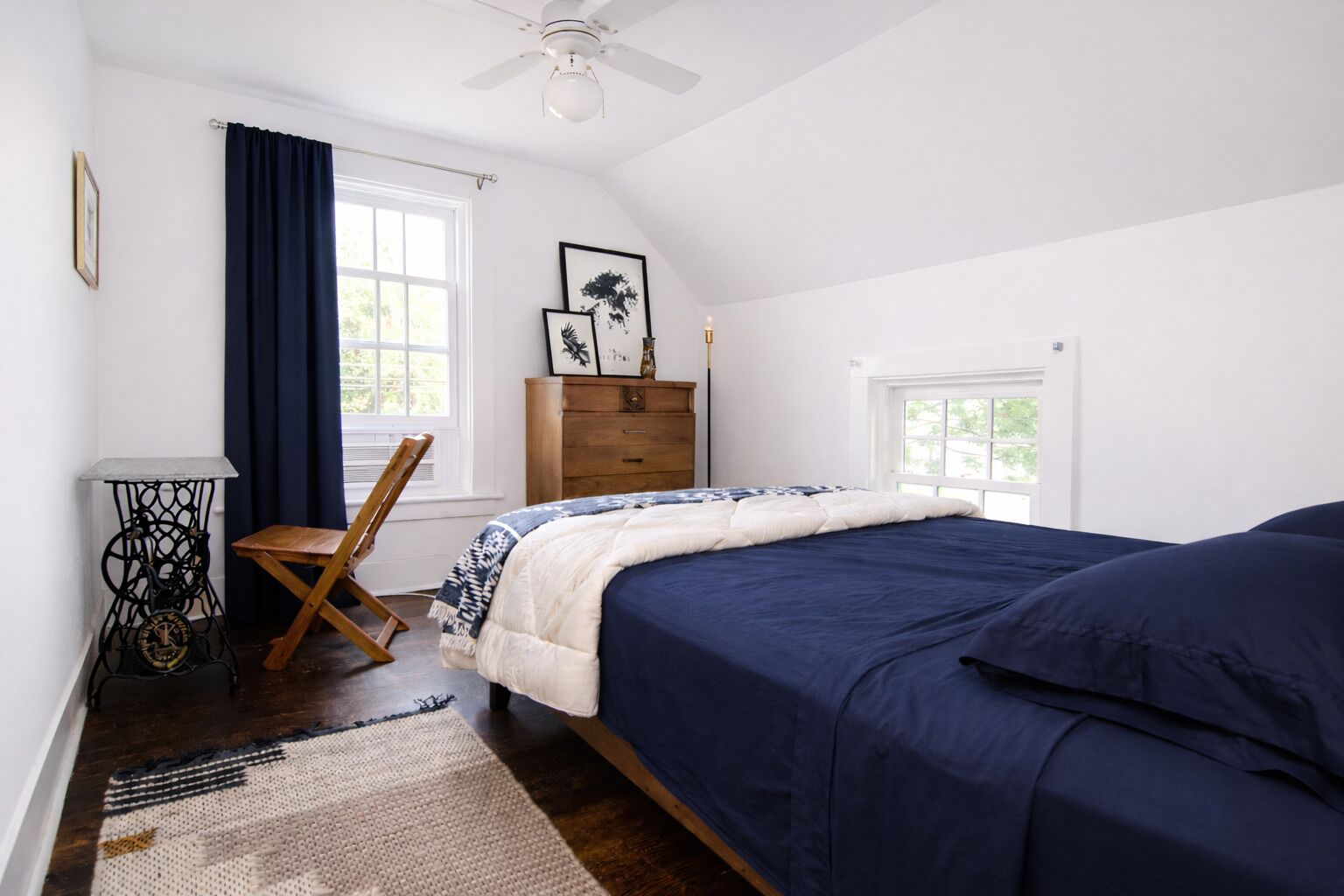 A bedroom with a bed, a chair, a sewing machine, a dresser, and a window.