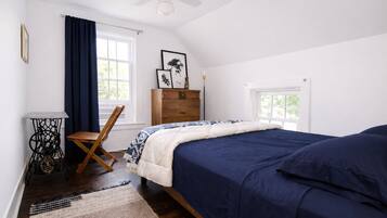 A bedroom with a bed, a chair, a sewing machine, a dresser, and a window.