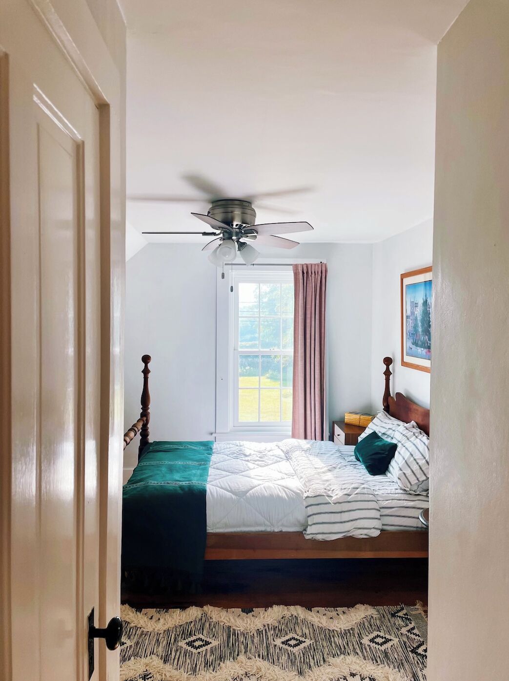 Une chambre à coucher avec un lit, un ventilateur de plafond, une fenêtre avec des rideaux, une porte et un tapis.