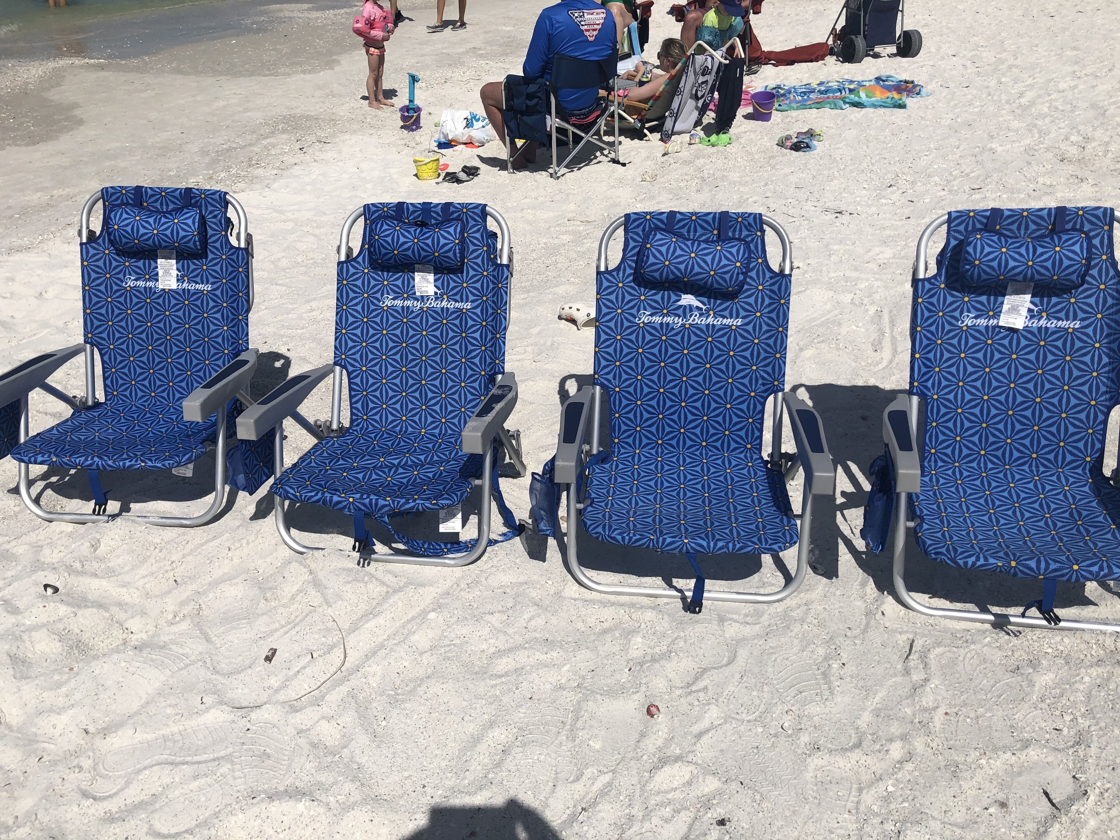 Quatre chaises de plage à motifs géométriques bleus, disposées en rangée sur une plage de sable.