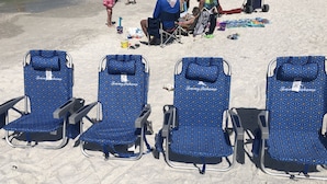 Vier Strandstühle mit blauem geometrischem Muster, an einer Reihe auf sandigem Strand platziert.