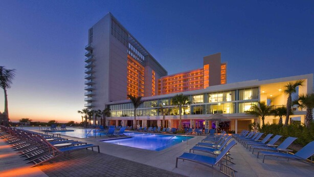 Ein Hotel mit Poolbereich, Liegestühlen und einem großen Mehrstöckiger Gebäude mit Balkonen.