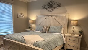 A bedroom with a wooden bed, two bedside tables with lamps, a decorative wall piece, and a framed quote on the wall. - Charming Retreat in Hallsville, TX – Your Cozy Home Away from Home! (Hallsville)