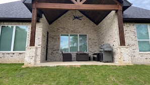 A covered patio area with a brick exterior, a ceiling fan, and a grill. - Charming Retreat in Hallsville, TX – Your Cozy Home Away from Home! (Hallsville)
