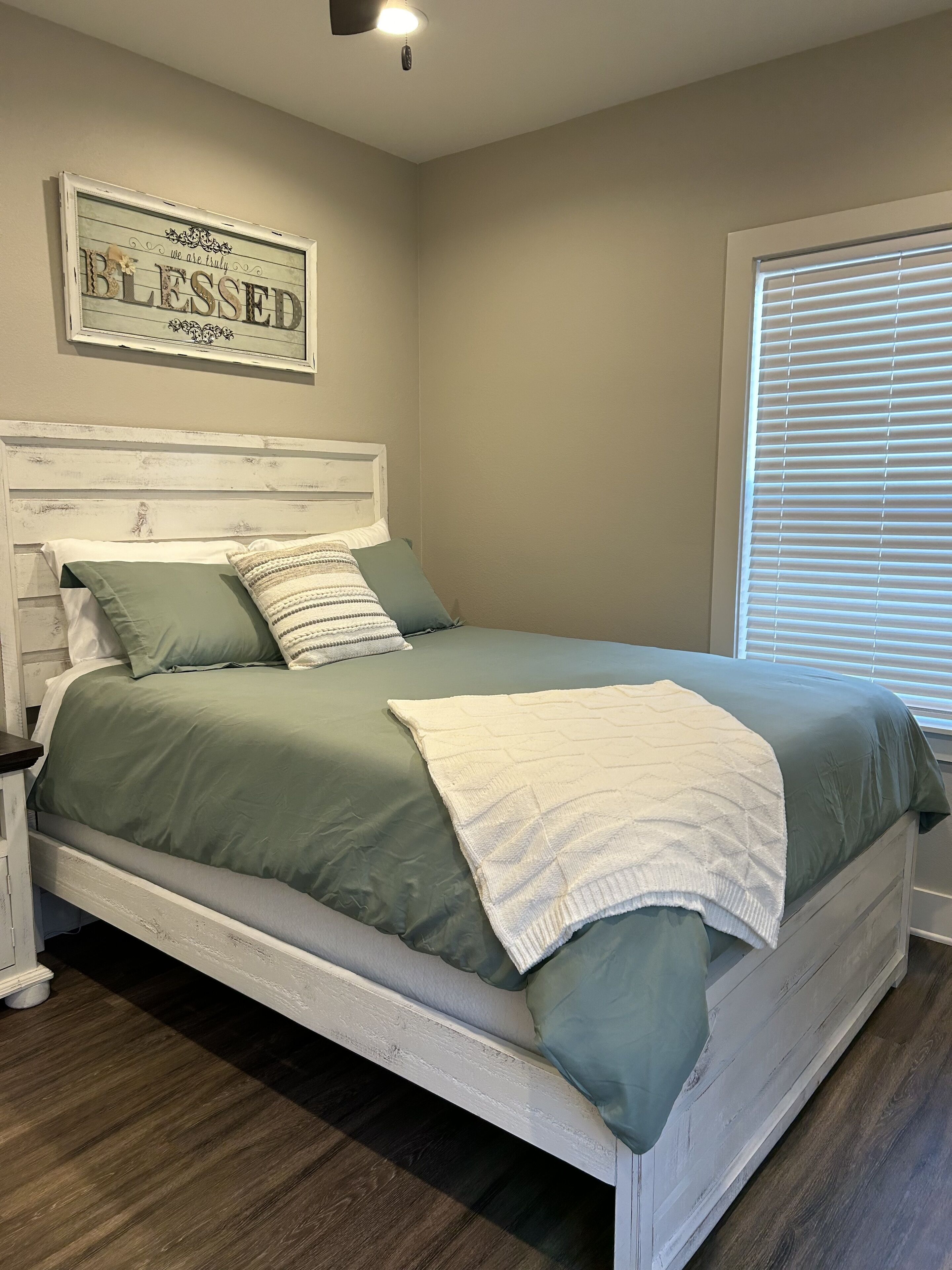 Quarto com cama branca, roupa de cama verde, cabeceira branca e um letreiro fixado na parede.