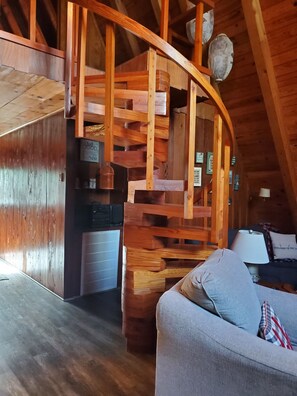 A wooden interior with a staircase, a sofa, and a kitchen area.
