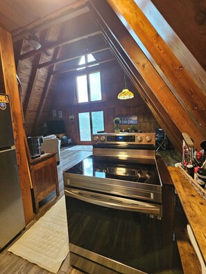 A kitchen with a stainless steel stove, wooden beams, and a window. - 2 wooded acres, 2 king beds & 1 full bed, fire pit & plenty of parking!  (Springville)