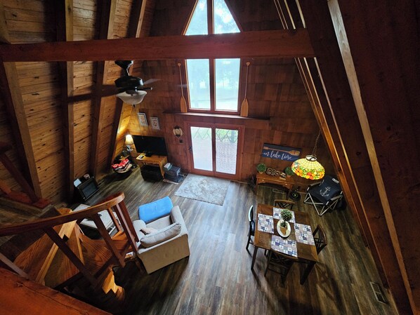 A cabin interior with a loft bedroom, a dining area, and a living room.
