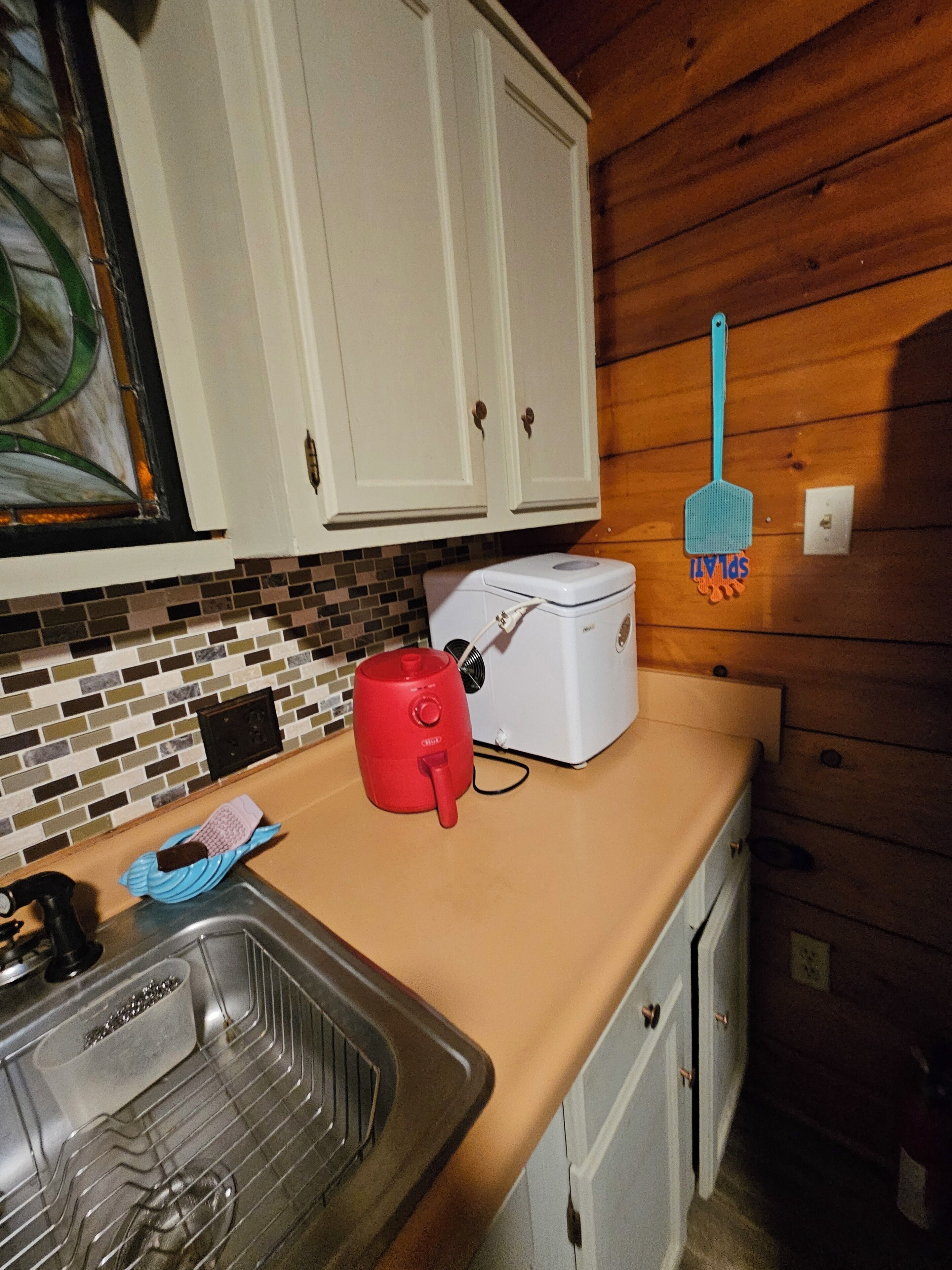 Een keuken met witte kastjes, een broodrooster, een rode waterkoker en een blauwe spons.