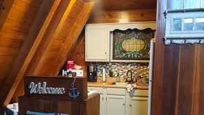 A wooden interior with a welcome sign, a kitchen area, and a view of the outside. - 2 wooded acres, 2 king beds & 1 full bed, fire pit & plenty of parking!  (Springville)