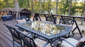 A wooden deck with a glass-top table and black metal chairs with patterned cushions. - 2 wooded acres, 2 king beds & 1 full bed, fire pit & plenty of parking!  (Springville)