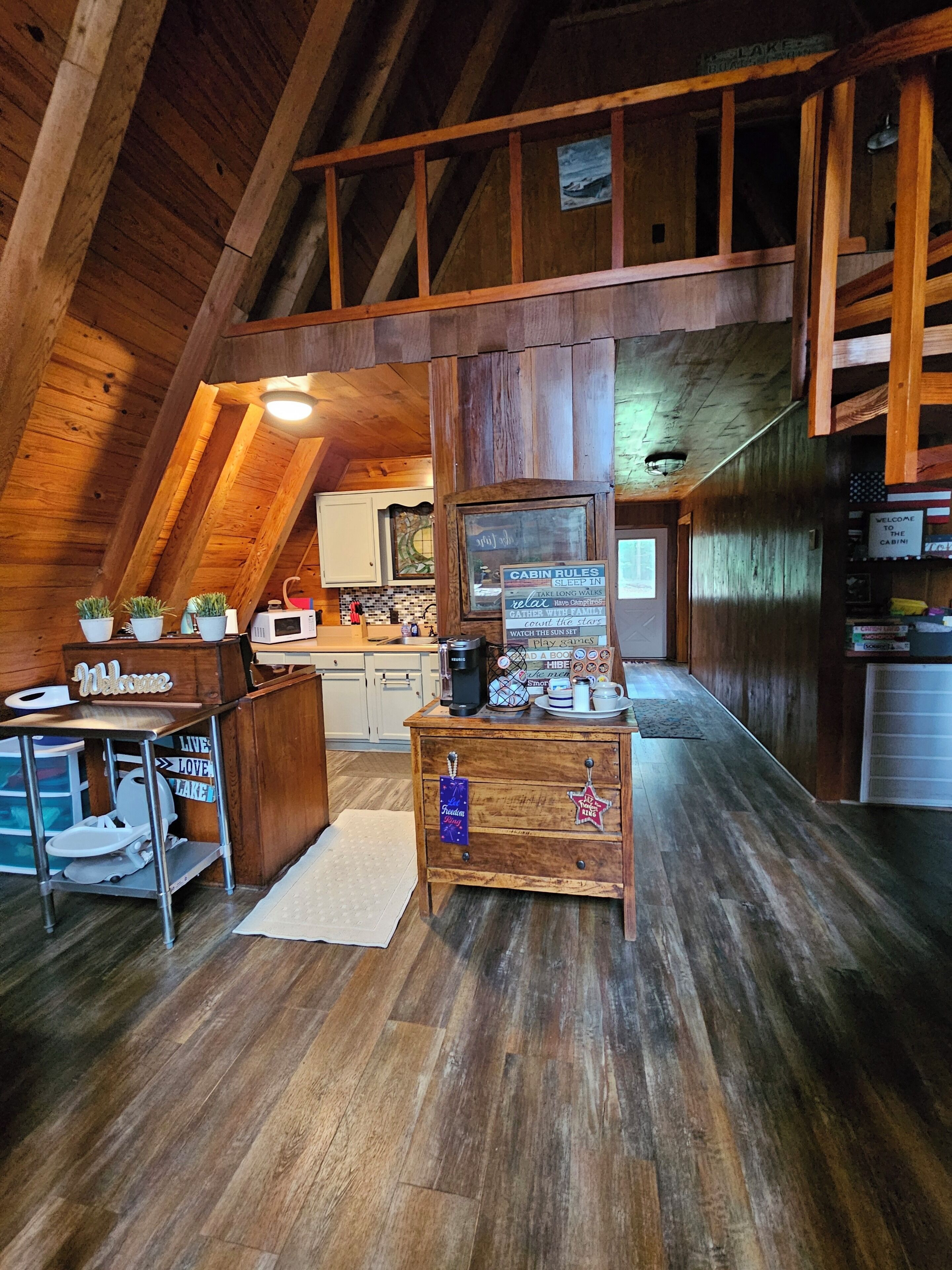 A cabin interior with a wooden ceiling, a kitchenette, a wooden cabinet with a sign, and a welcome sign.