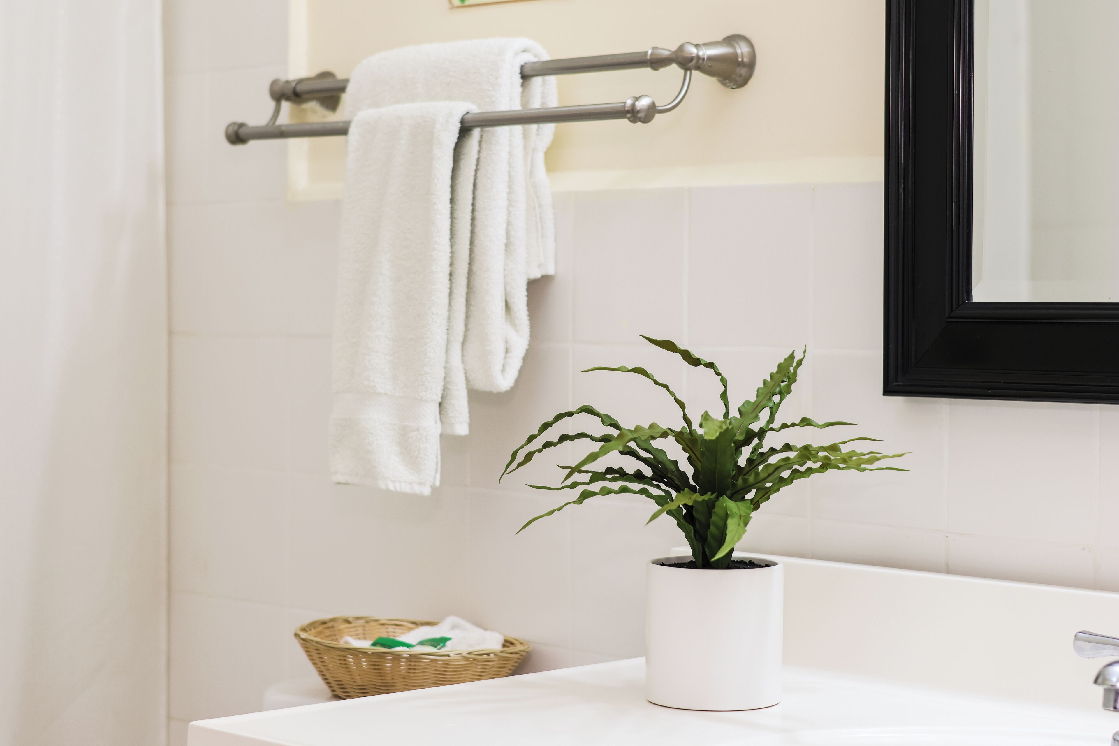 A bathroom with a white sink, a potted plant, a towel rack with white towels, and a framed mirror.