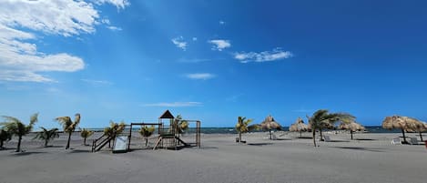 A beach with thatched umbrellas, palm trees, and a wooden structure.