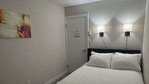 A bedroom with a bed, two wall-mounted lights, a door, and a painting on the wall.