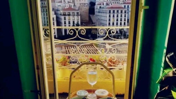 A balcony with a table set for two, a bottle of water, and a view of a cityscape.