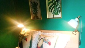 A bed with floral bedding, two pillows with tropical prints, and a nightstand with a lamp.