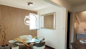 A modern dining area with a glass table and wooden chairs, a vertical wooden panel wall, and a mirror on the wall.