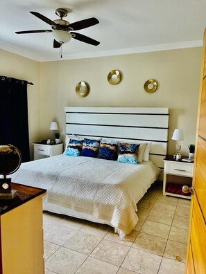 A bedroom with a bed, nightstands, a ceiling fan, and decorative wall plates. - Central to Everything Steps from Beach (Punta Cana)