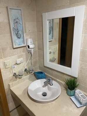 A bathroom with a sink, a mirror, a hairdryer, a blue soap dish, and a small potted plant. - Central to Everything Steps from Beach (Punta Cana)
