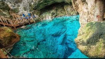 Una piscina azul cristalina con una terraza de madera y sillas, rodeada de acantilados rocosos.