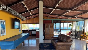 Un amplio salón con mesa de billar, un sofá de cuero y vista al océano.