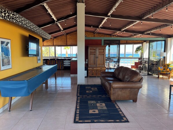 Un amplio salón con mesa de billar, un sofá de cuero y vista al océano.