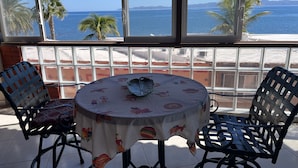 Una mesa con mantel floreado y dos sillas, con vista a una playa con palmeras y el océano.