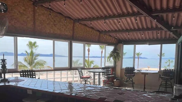 Un espacio de comedor al aire libre cubierto, con vista al mar y palmeras.