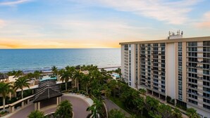 A high-rise hotel with a pool and palm trees, overlooking a beach and ocean.