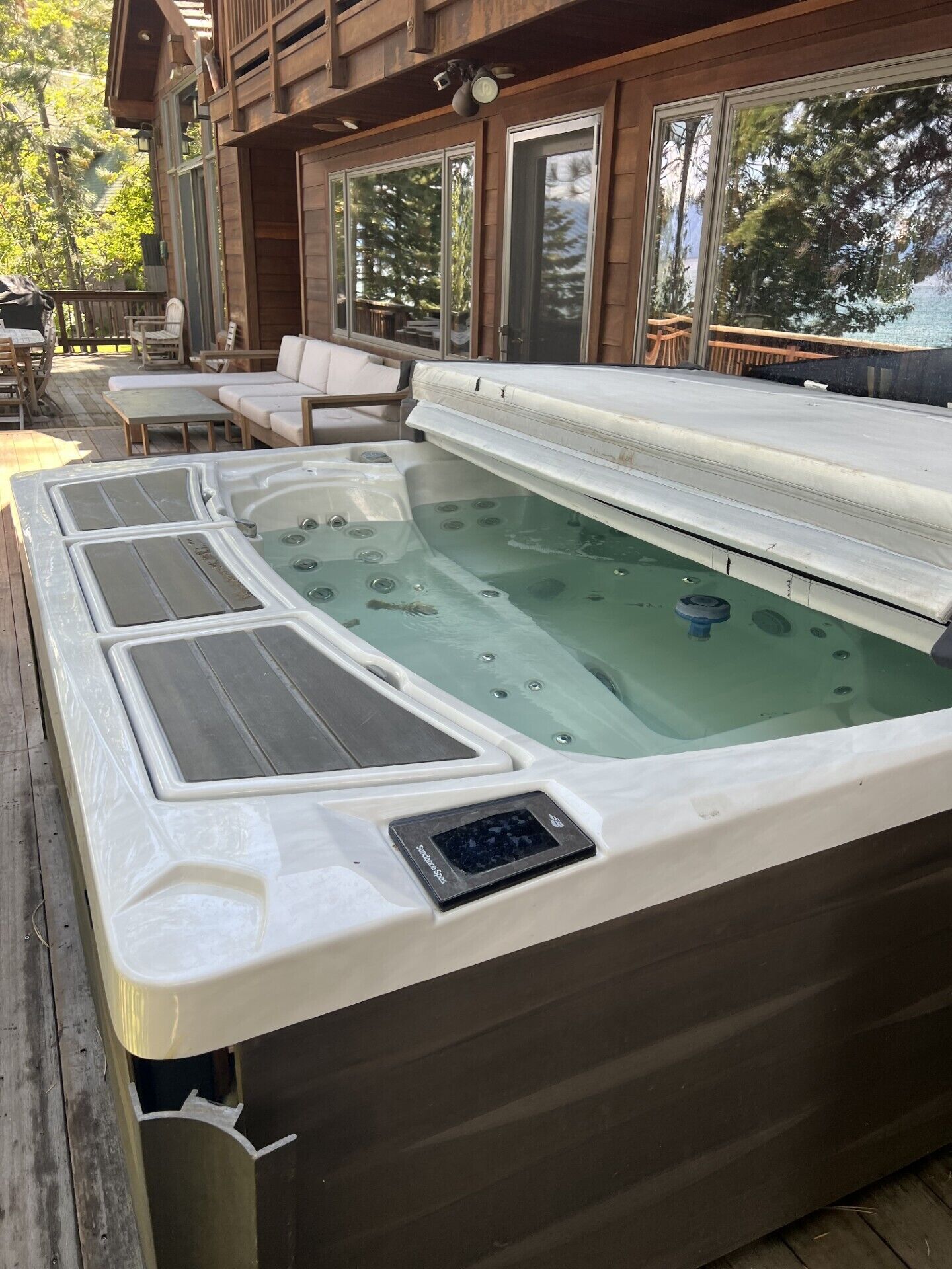 A hot tub on a wooden deck with a view of a lake and a building with large windows.