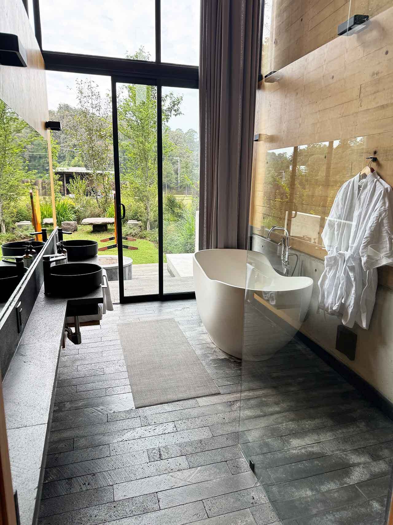 Un bagno moderno con una vasca freestanding, una grande finestra e vista su un giardino.