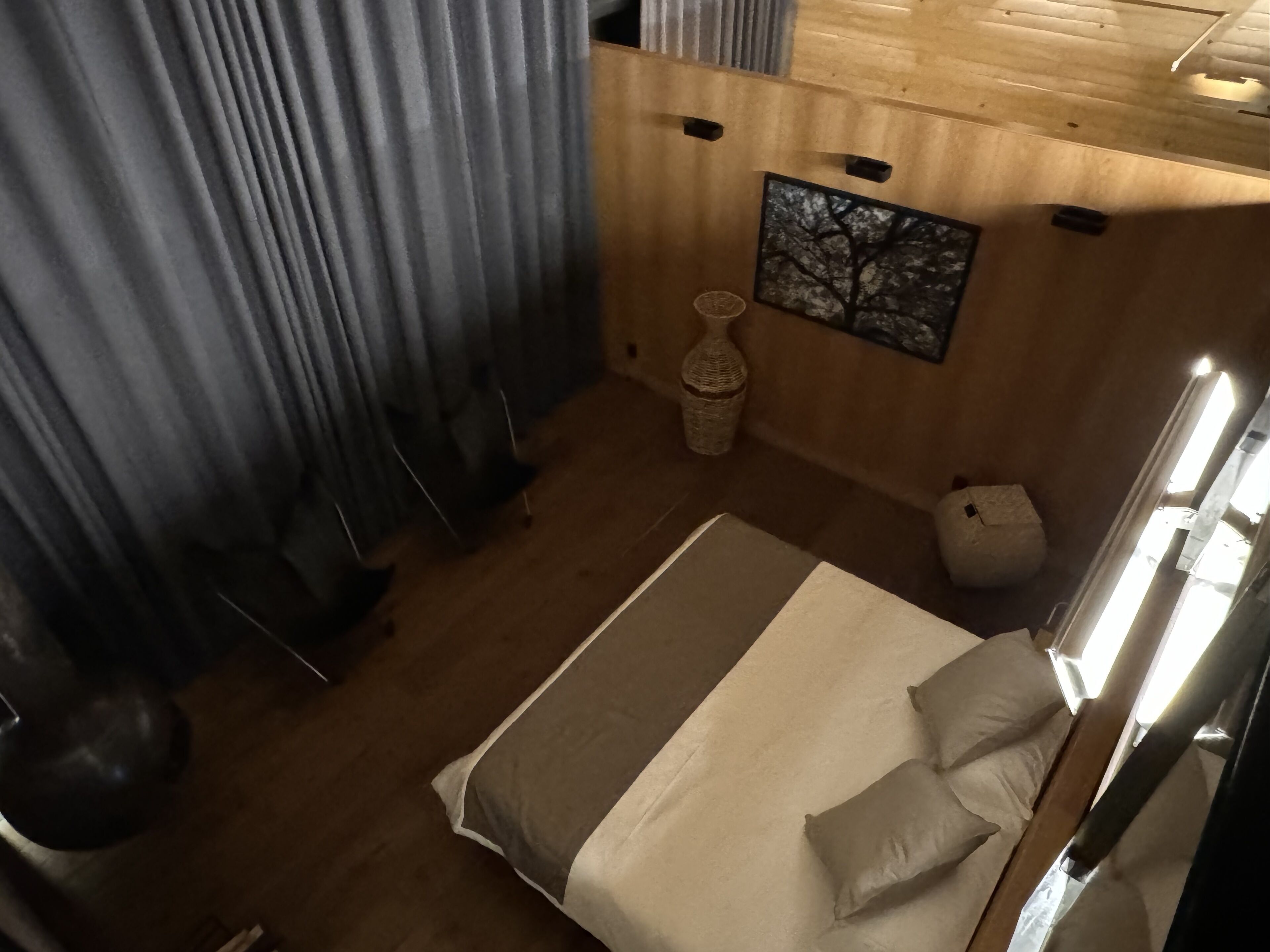 A bedroom with a bed, curtains, a wall-mounted artwork, a small vase, and a wooden headboard.