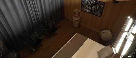 A bedroom with a bed, curtains, a wall-mounted artwork, a small vase, and a wooden headboard.