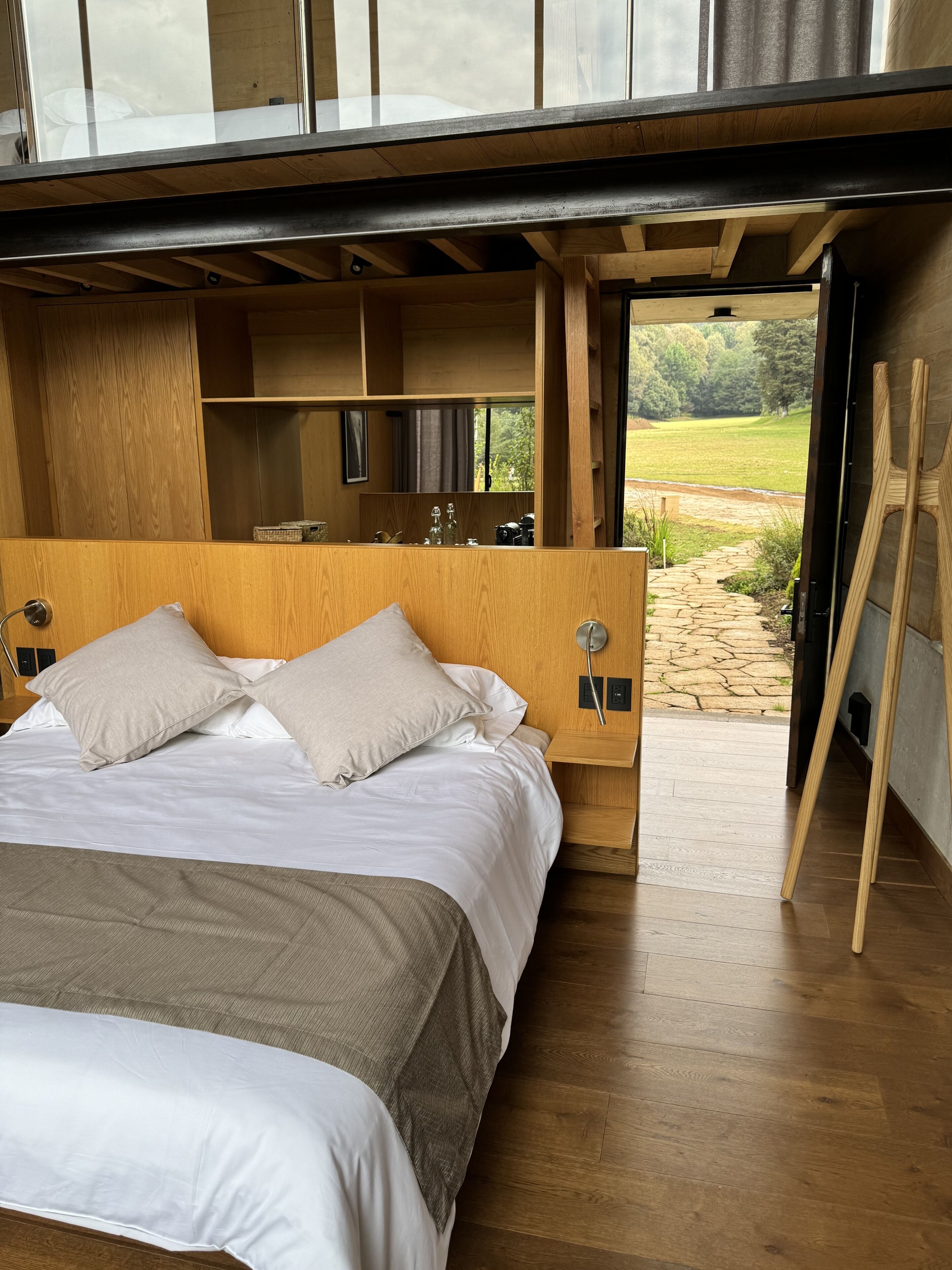A modern bedroom with a large bed, wooden headboard, and a view of the outdoors.