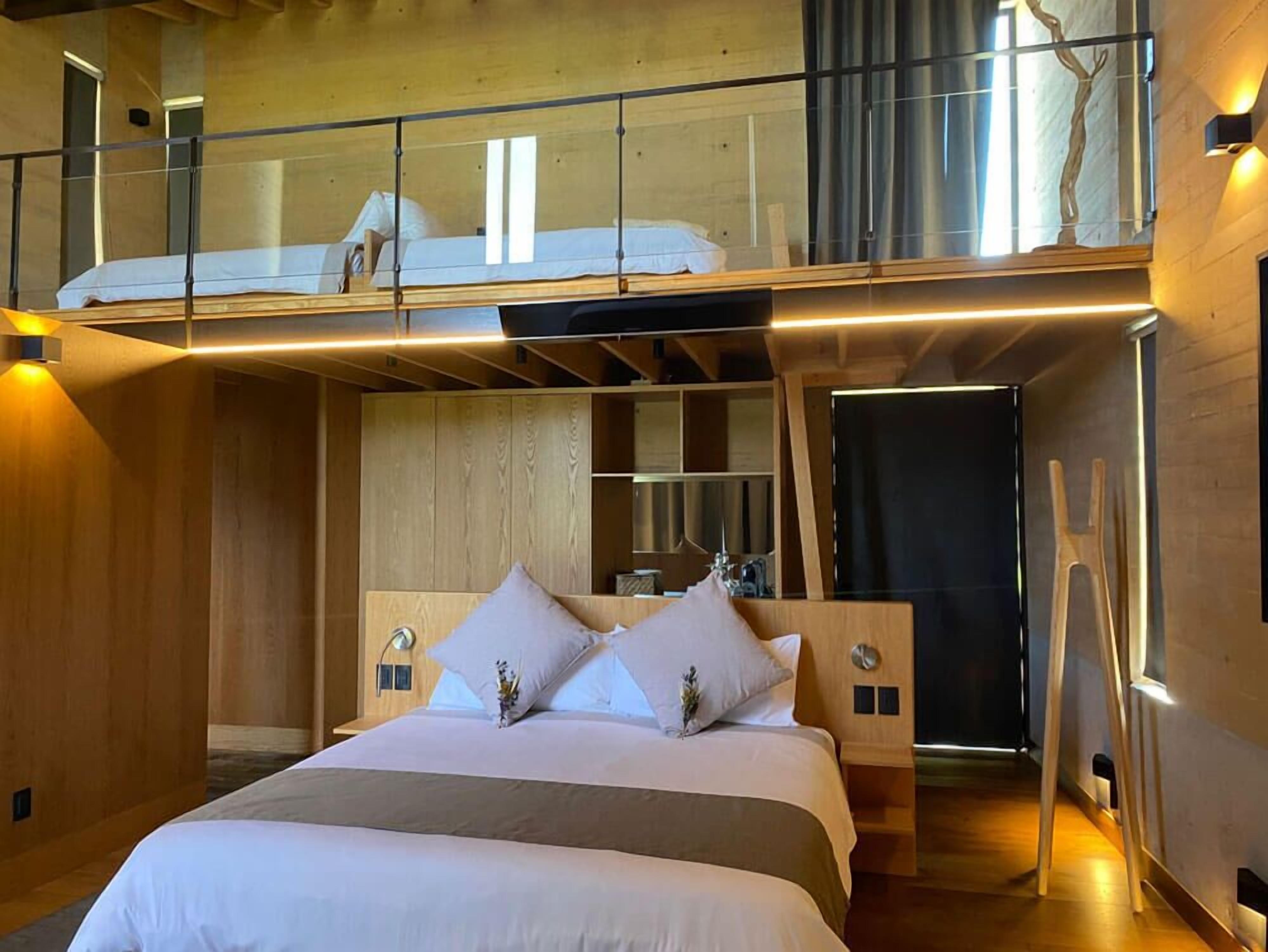 Une chambre moderne avec un grand lit, une tête de lit en bois et un espace en mezzanine situé au-dessus.