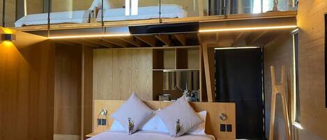 Une chambre moderne avec un grand lit, une tête de lit en bois et un espace en mezzanine situé au-dessus.