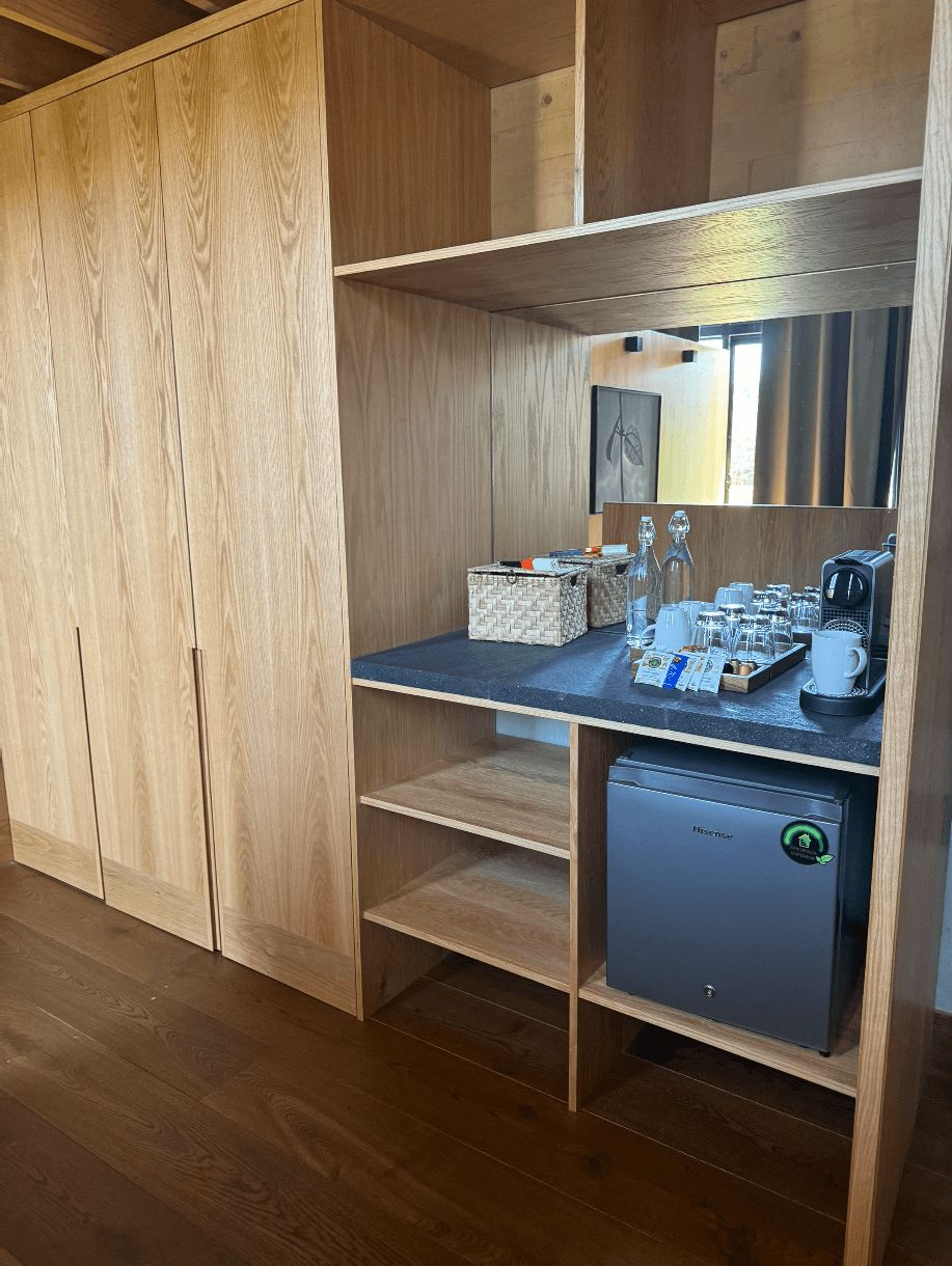 Een houten garderobe met een geïntegreerd bureau, een kleine koelkast en een spiegel.