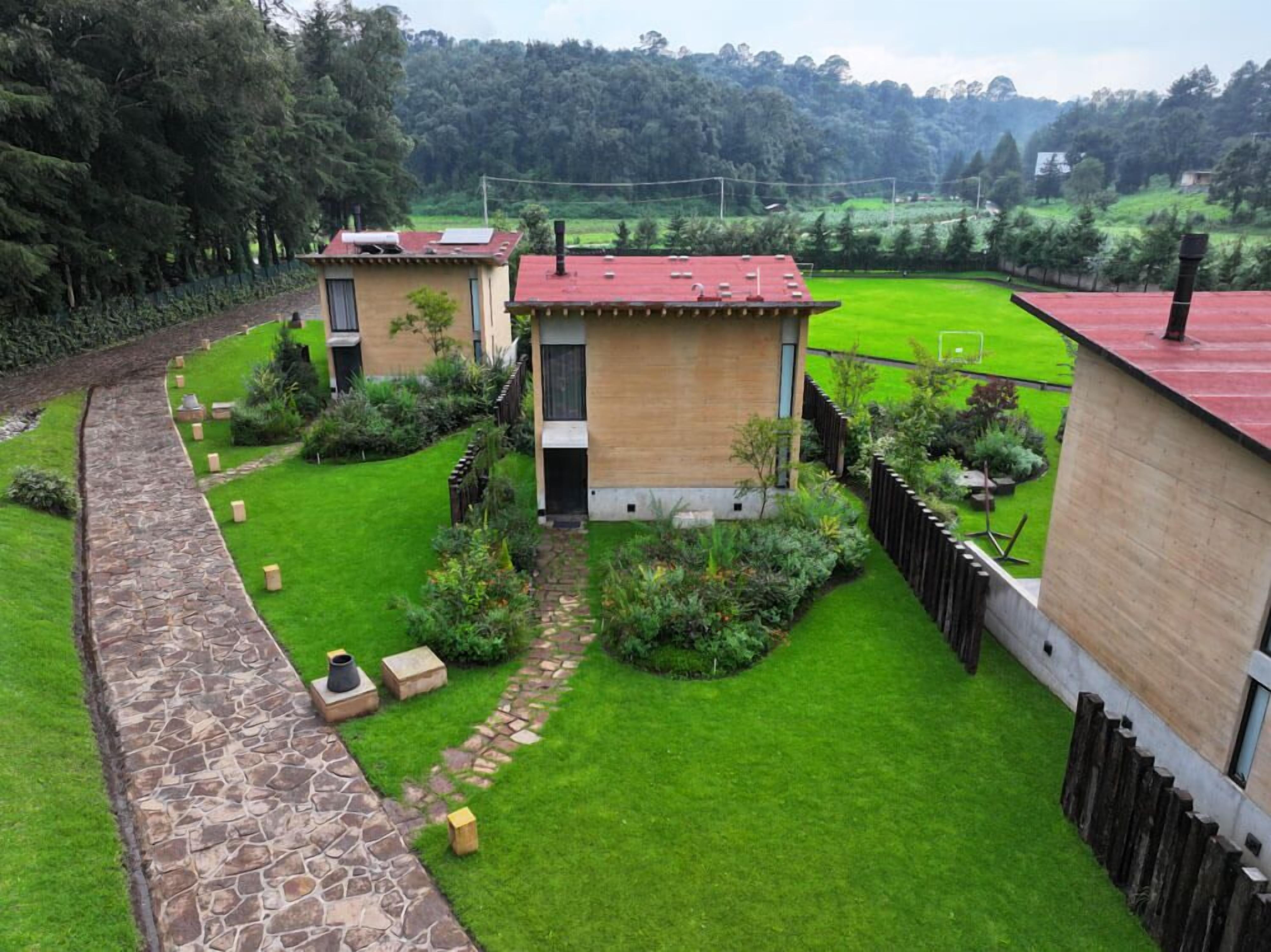 A modern house with a stone pathway leading to a wooden door, surrounded by lush green lawns and a fenced garden.