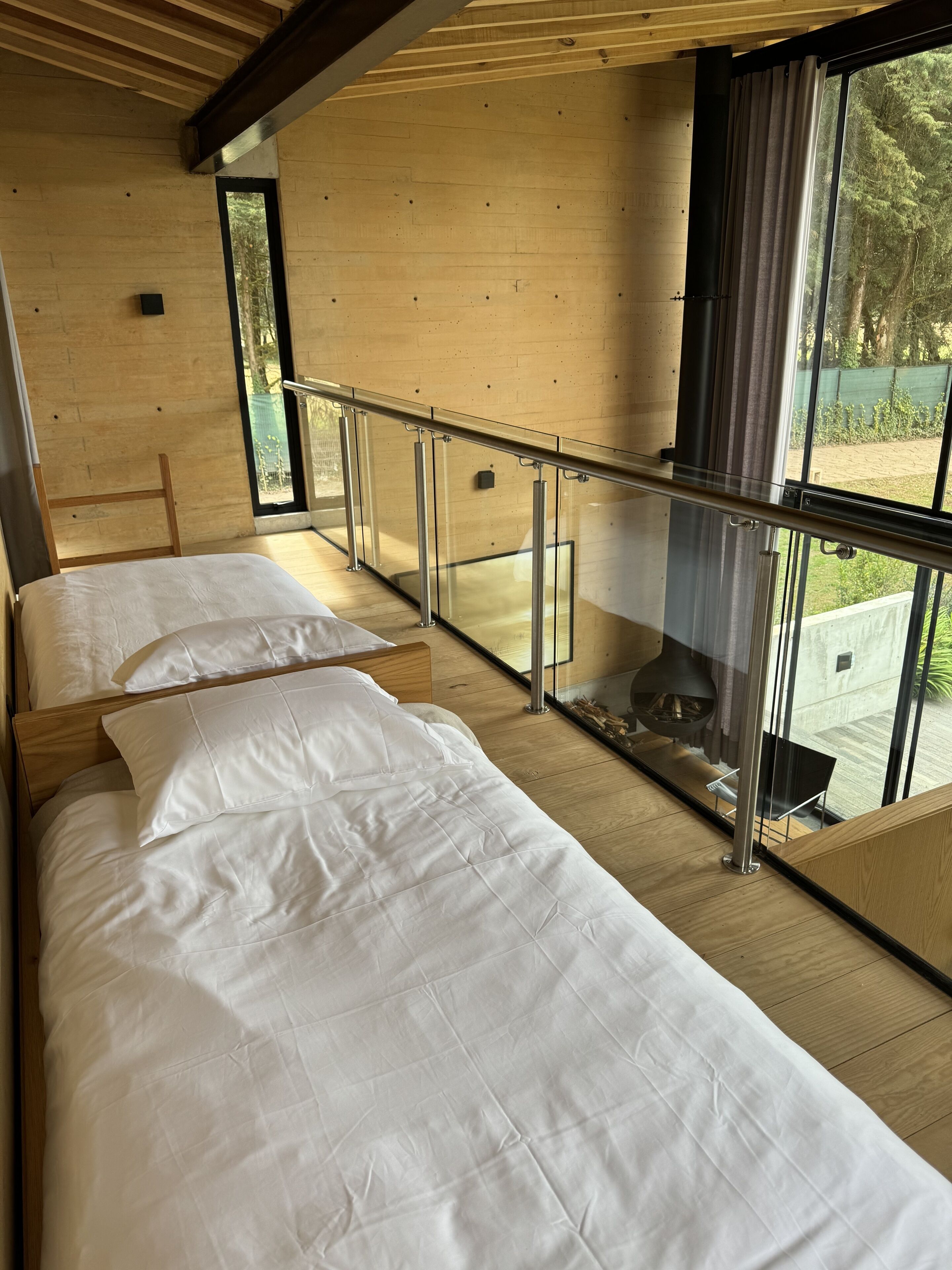 Un dormitorio moderno con dos camas, un balcón de cristal y vistas al exterior.