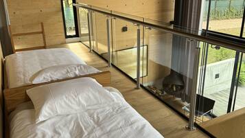 Un dormitorio moderno con dos camas, un balcón de cristal y vistas al exterior.