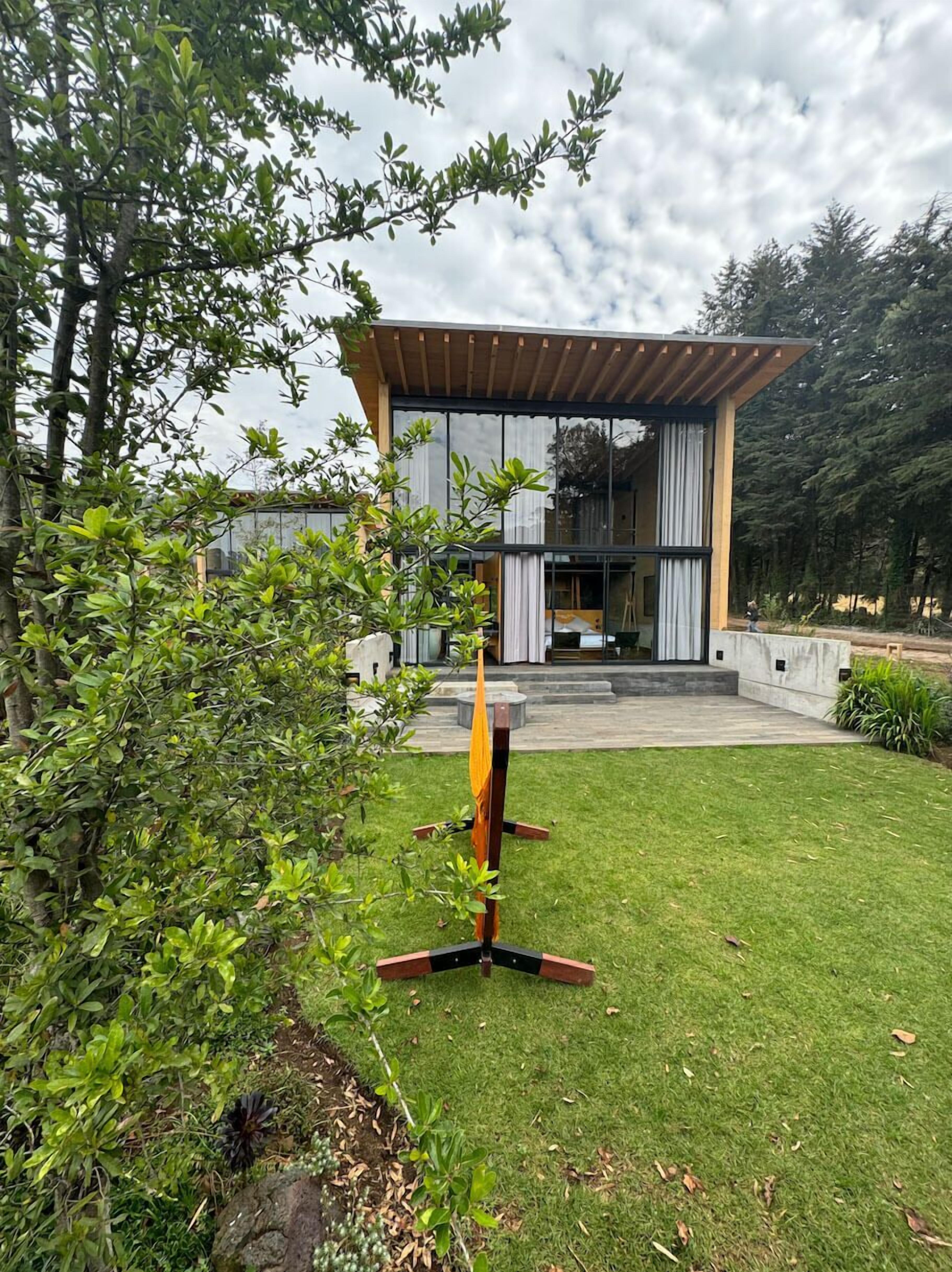 A modern house with a large glass facade, a wooden pergola, and a well-maintained lawn.