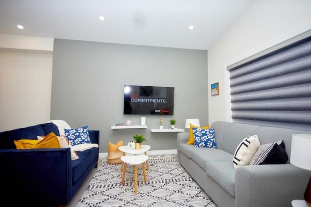 A modern living room with a grey sofa, a blue sofa, a small white table, and a TV mounted on the wall.