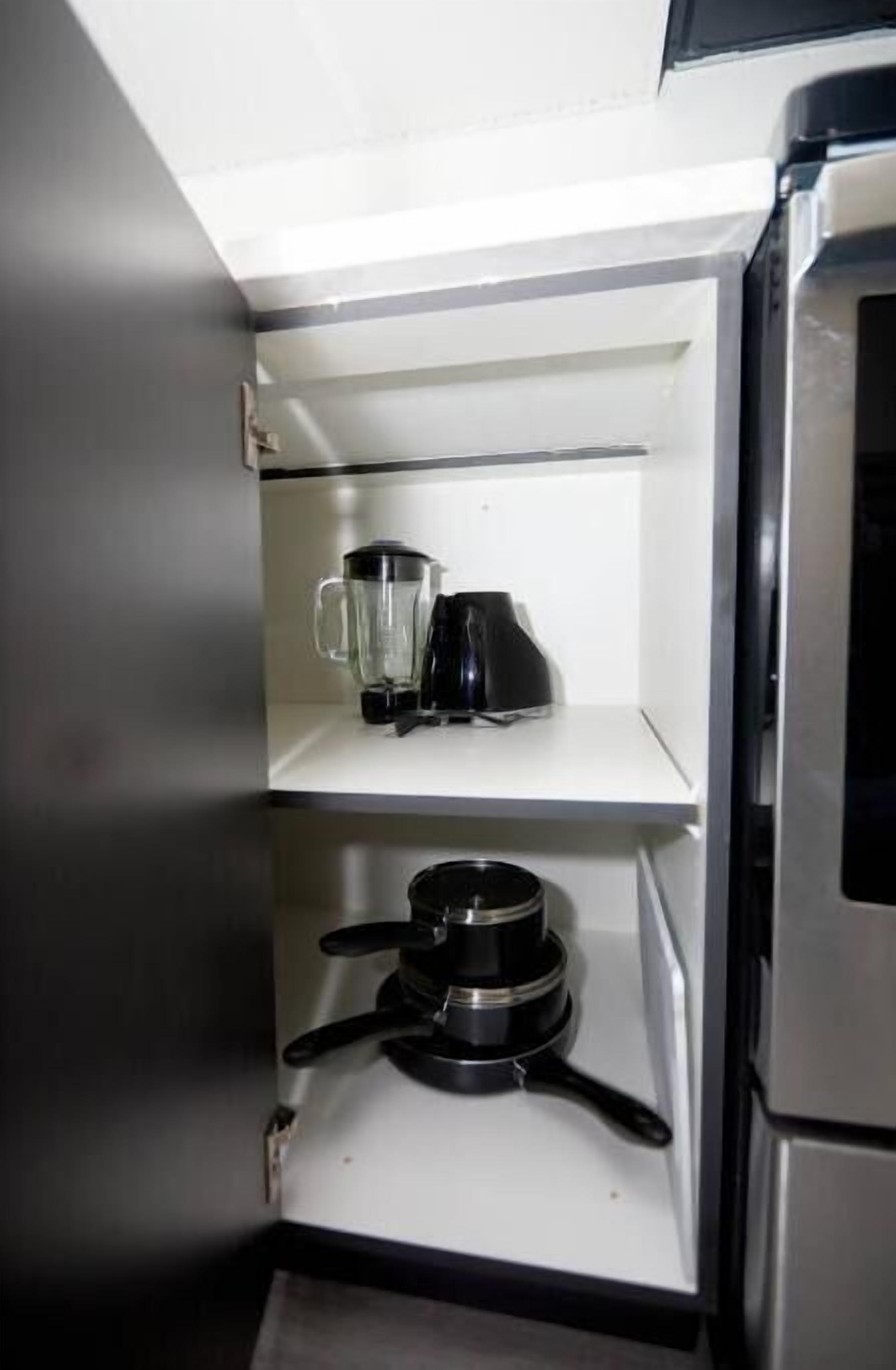 A compact kitchen with a blender, a coffee maker, and a frying pan on the counter.