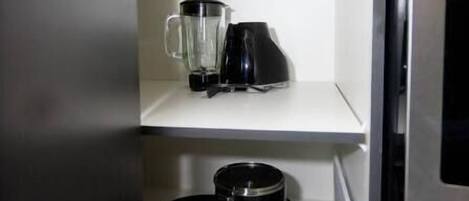 A compact kitchen with a blender, a coffee maker, and a frying pan on the counter.