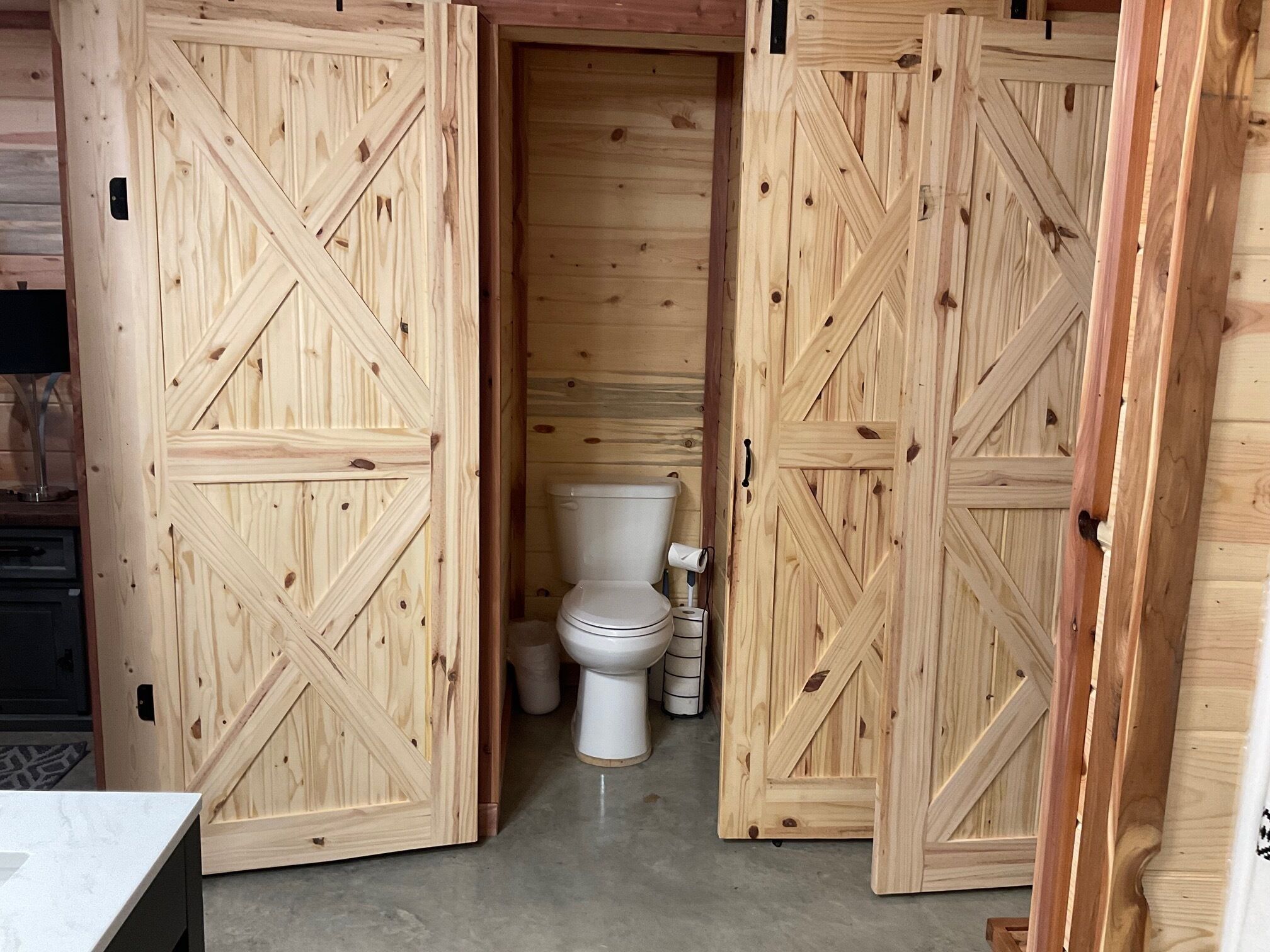 Un baño de madera con inodoro, un cesto de basura y una puerta de madera con un diseño geométrico.