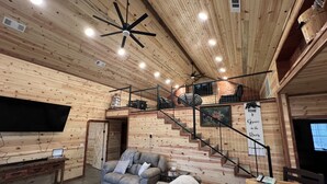Un vaste espace de vie doté d’un haut plafond, de murs en bois, d’un escalier, d’un téléviseur à écran plat et d’un coin salon confortable.